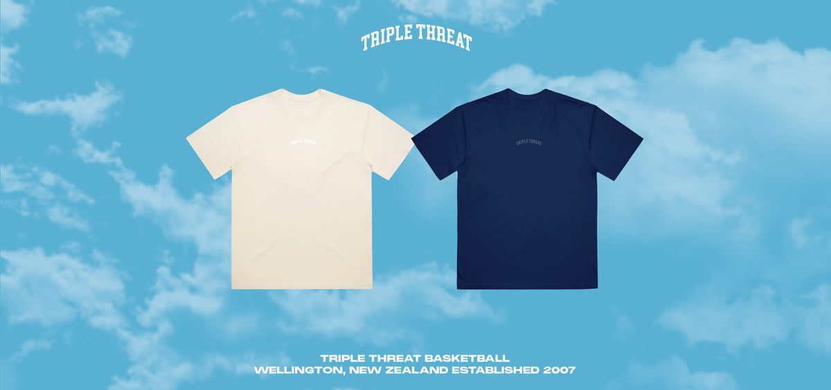 Two t-shirts, one cream and one navy, on a blue sky background with 'Triple Threat' branding.