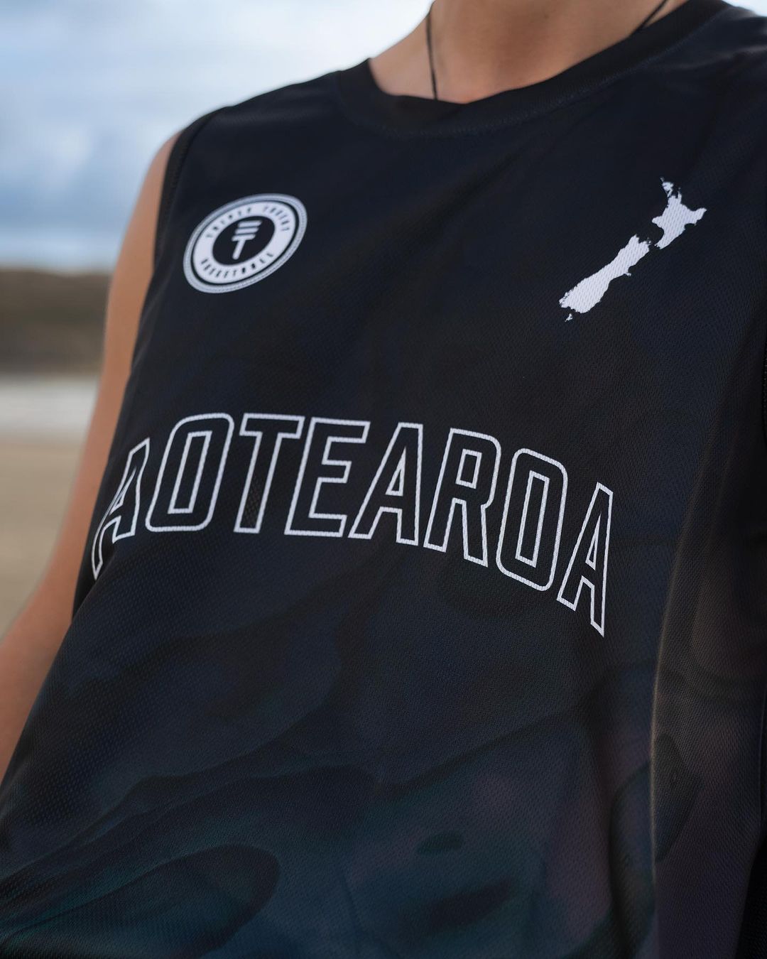 Close-up of basketball singlet with New Zealand map and Paua design with Triple Threat logo on the shoulder and "Aotearoa" text in the middle, all in white
