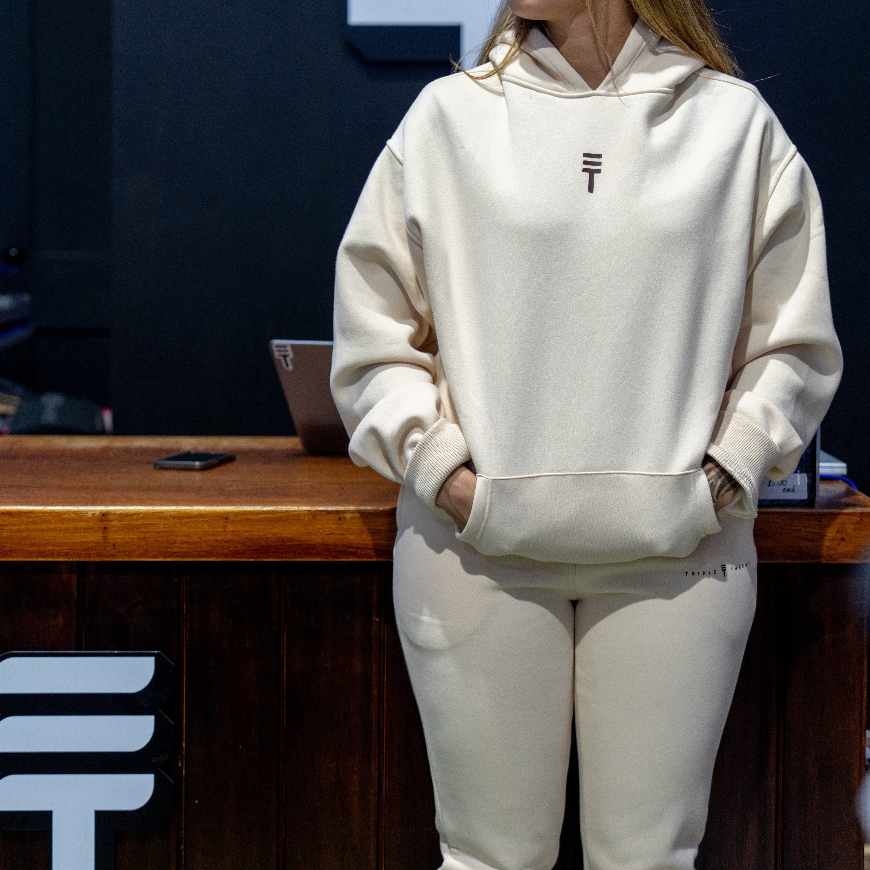 Model wearing a cream Triple Threat hoodie in front of a dark background