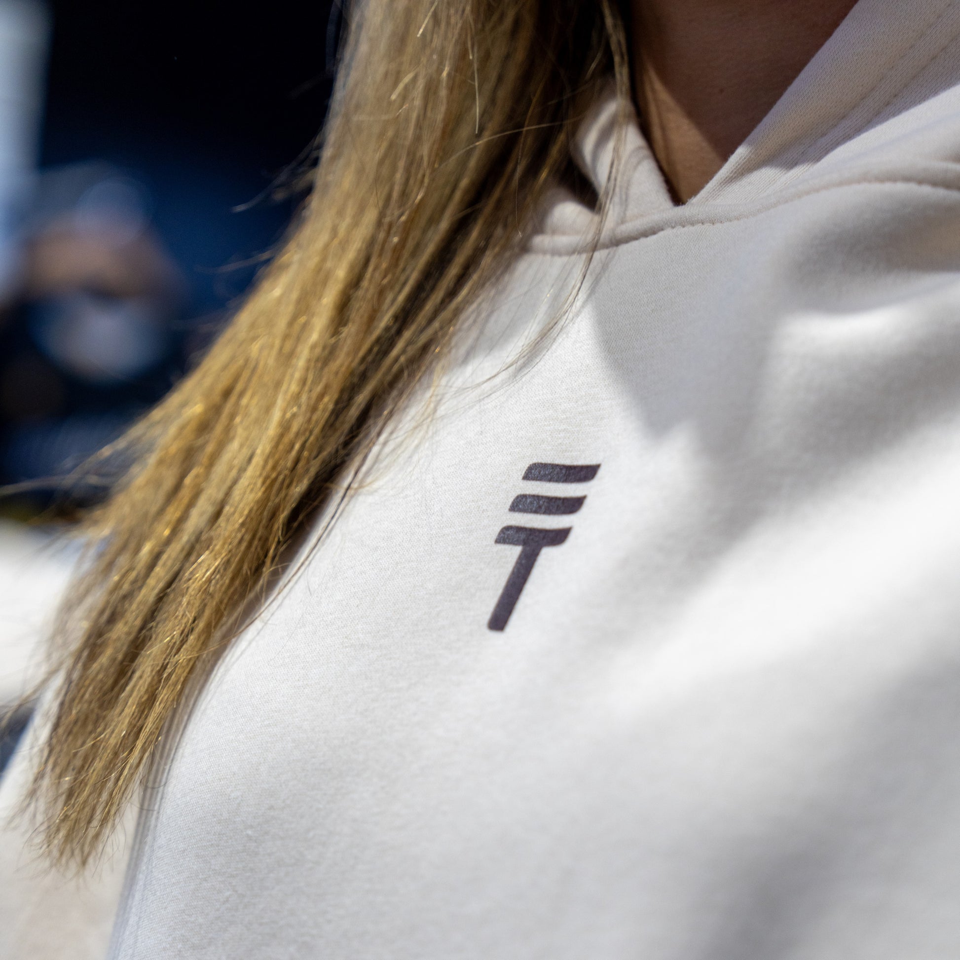Close-up of a person wearing a cream hoodie with Triple Threat logo on the chest.