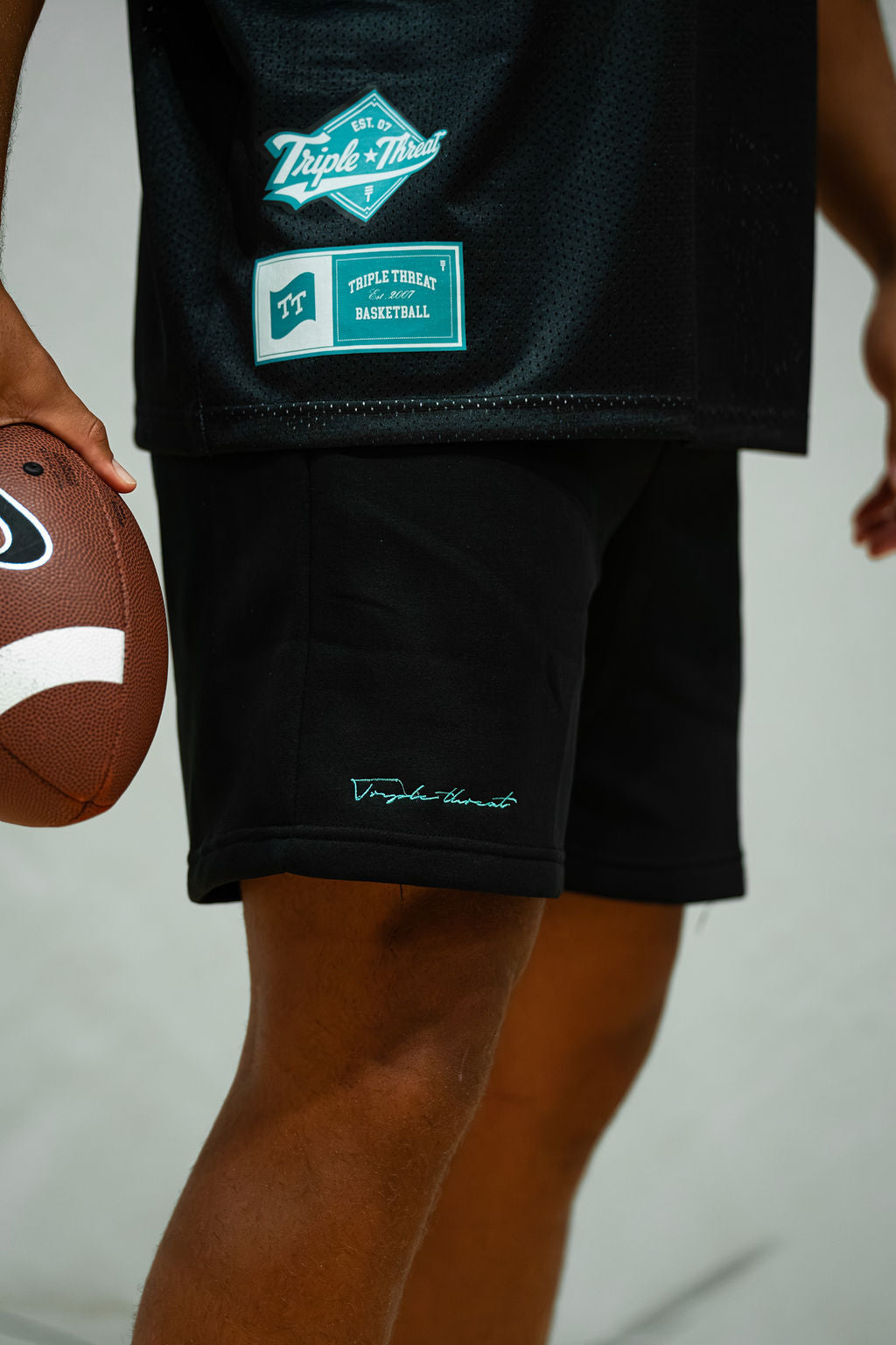 Person wearing black fleece shorts with green script logo on a plain background