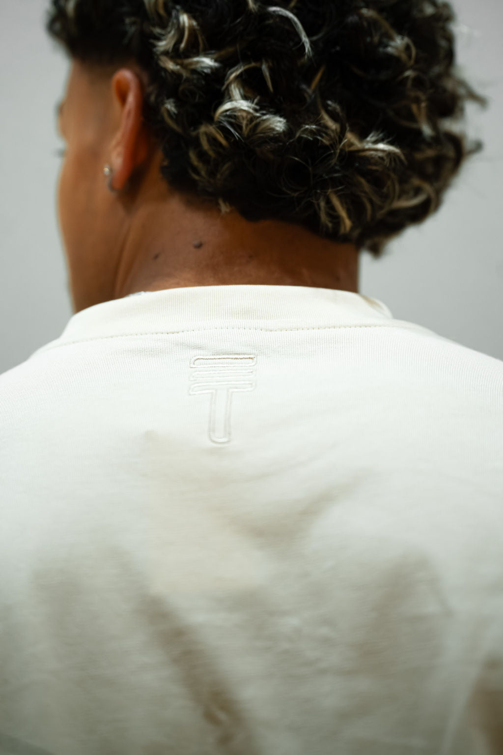 Person wearing a cream t-shirt with Triple Threat logo on the back, facing away from the camera.