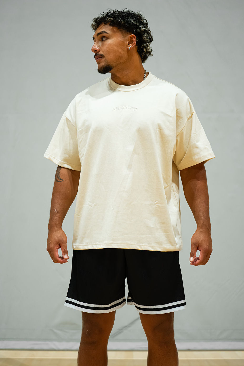 Man wearing a cream oversized t-shirt and black shorts with white trim against a grey background