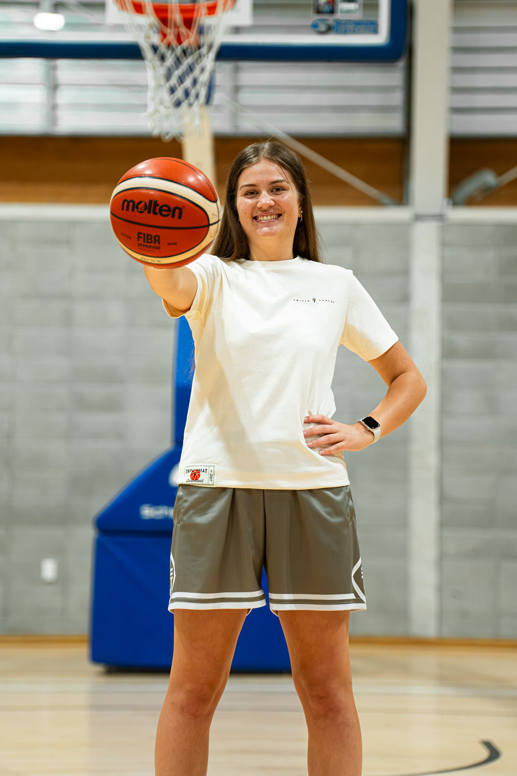 Woman in cream t-shirt holding a basketball in a gymnasium