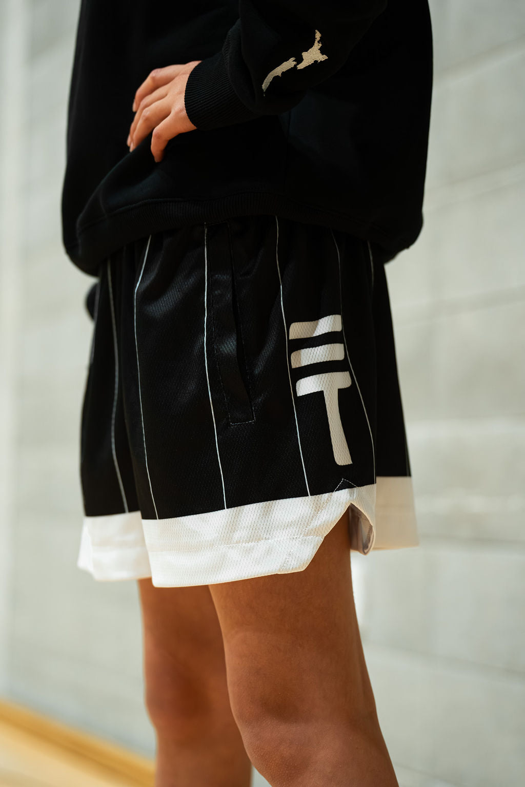 Person wearing a black sweatshirt with white accents and kids kiwi shorts in black against a neutral background