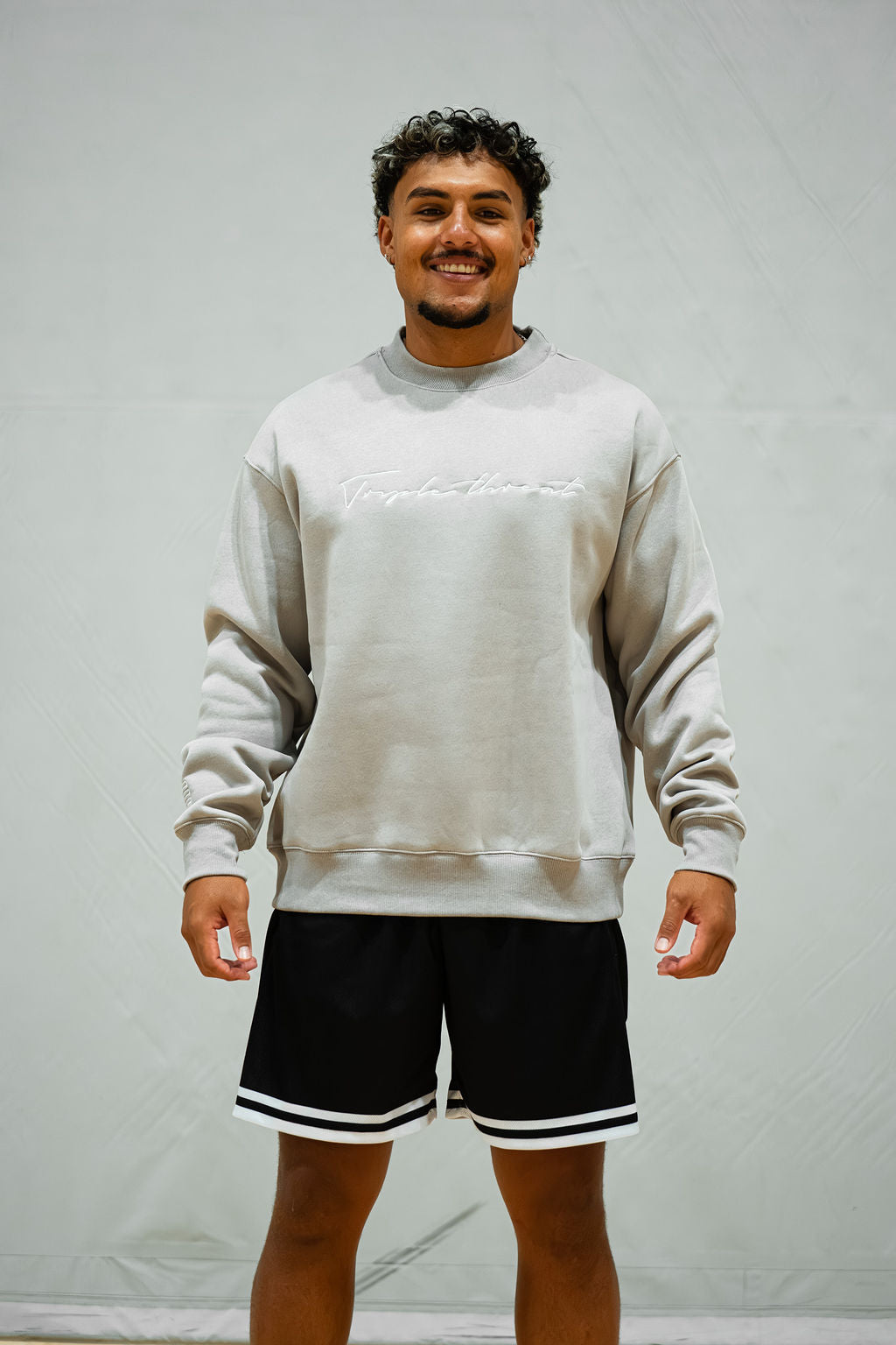 Man wearing a light grey sweatshirt and black basketball shorts with white trim against a plain background