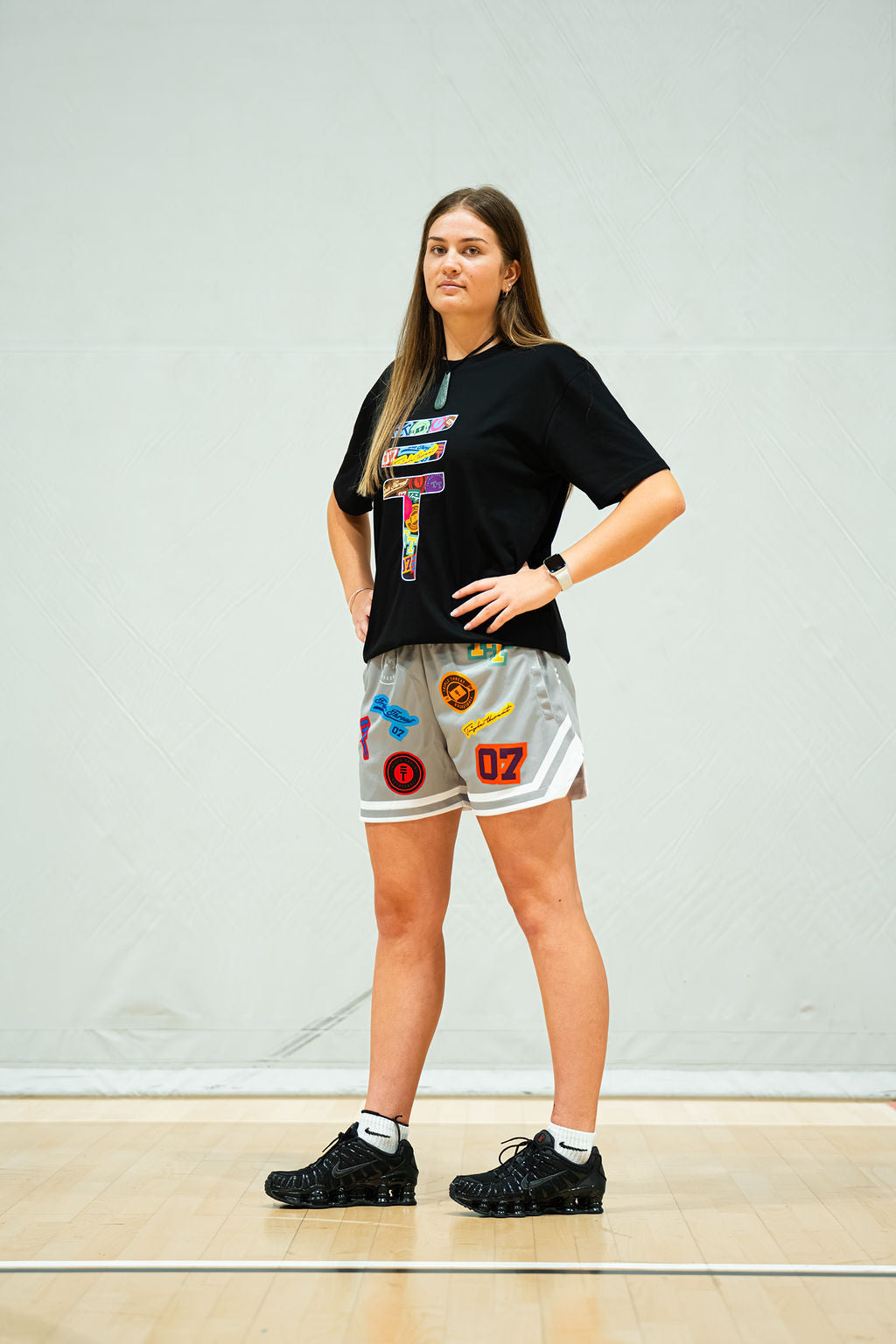 Person wearing a black t-shirt with colorful graphics and grey shorts with colorful designs on a light background