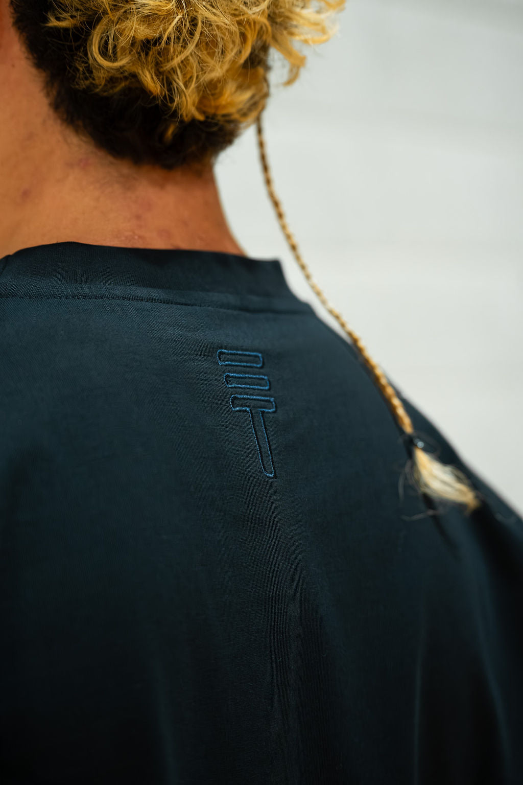 Man wearing a dark navy blue t-shirt with a logo on the back against a light background