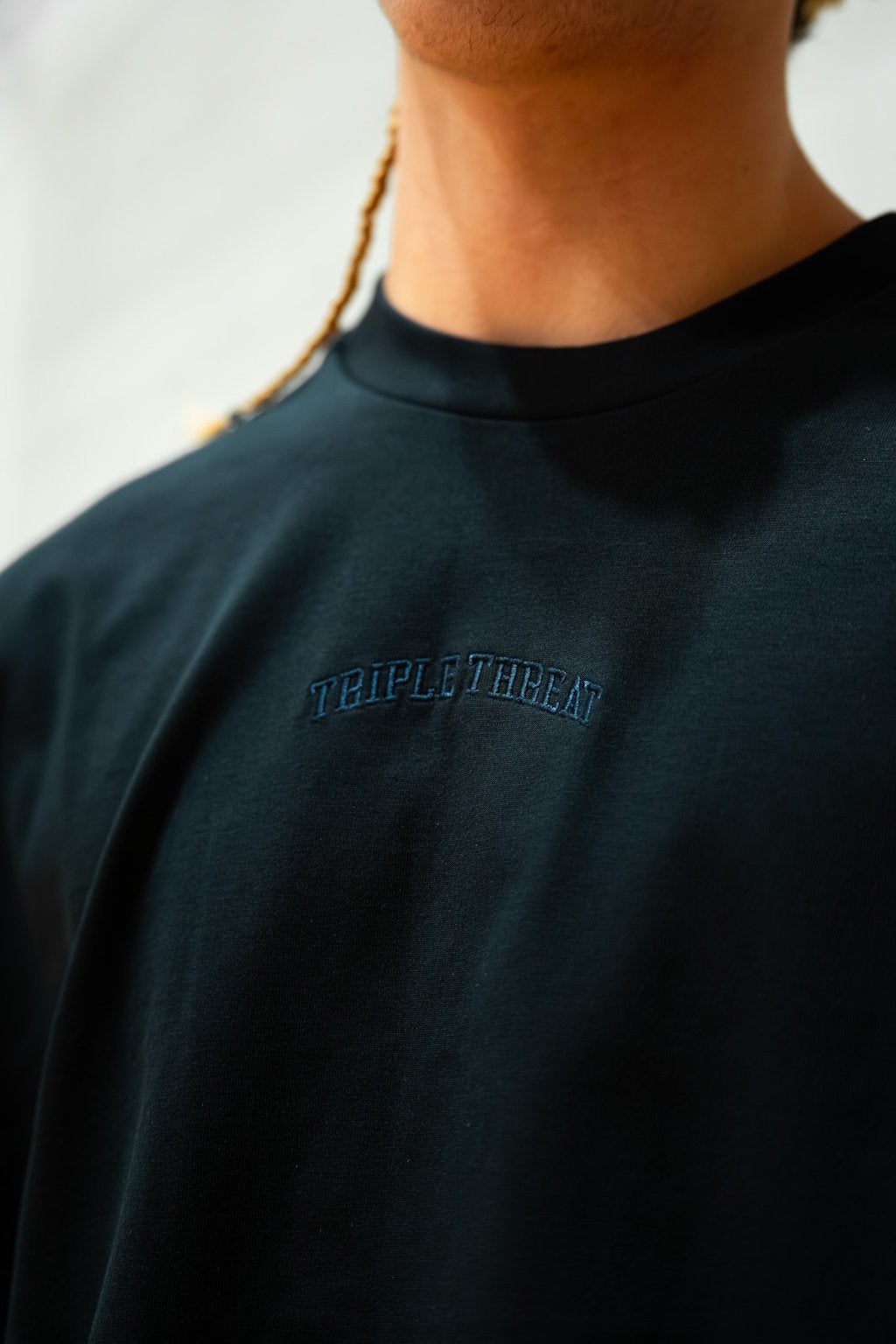 Person wearing a dark navy blue t-shirt with 'TRIPLE THREAT' logo on a blurred background