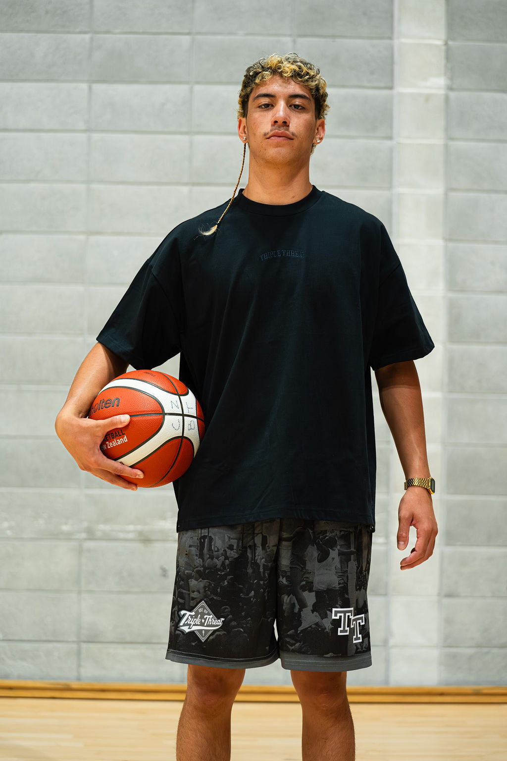 Man holding a basketball indoors in a dark navy tee with a neutral background