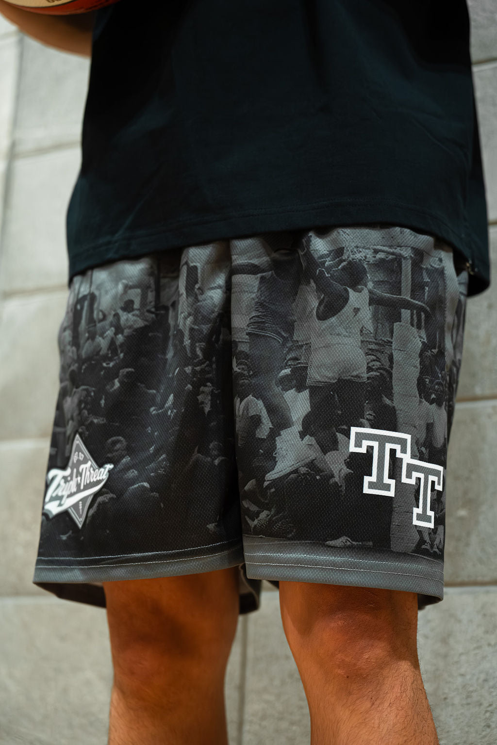 Person wearing black basketball shorts with rucker park pattern and logo, standing against a light-colored wall.