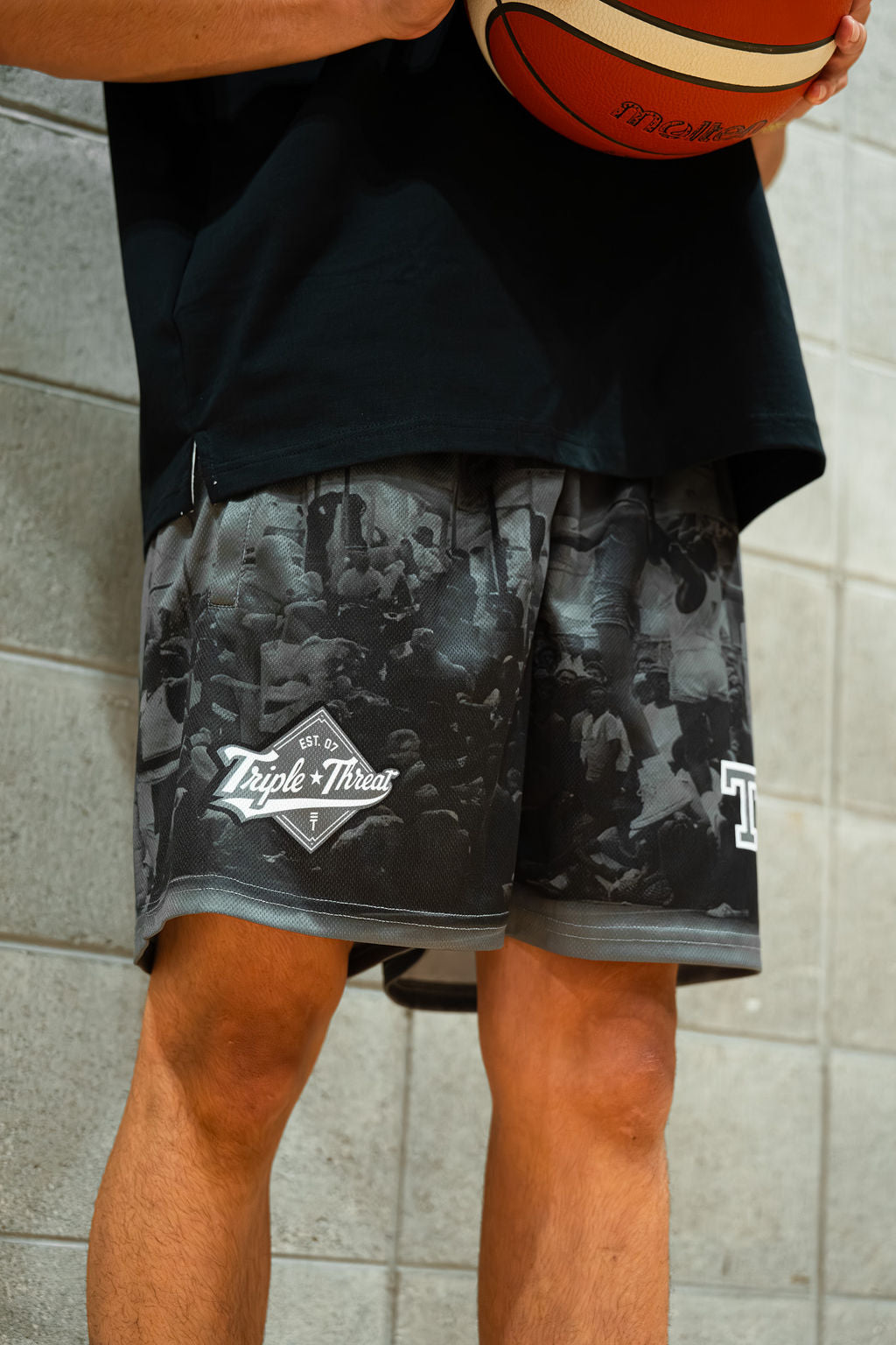 Person wearing rucker black basketball shorts with Triple Threat brand logo, holding a basketball