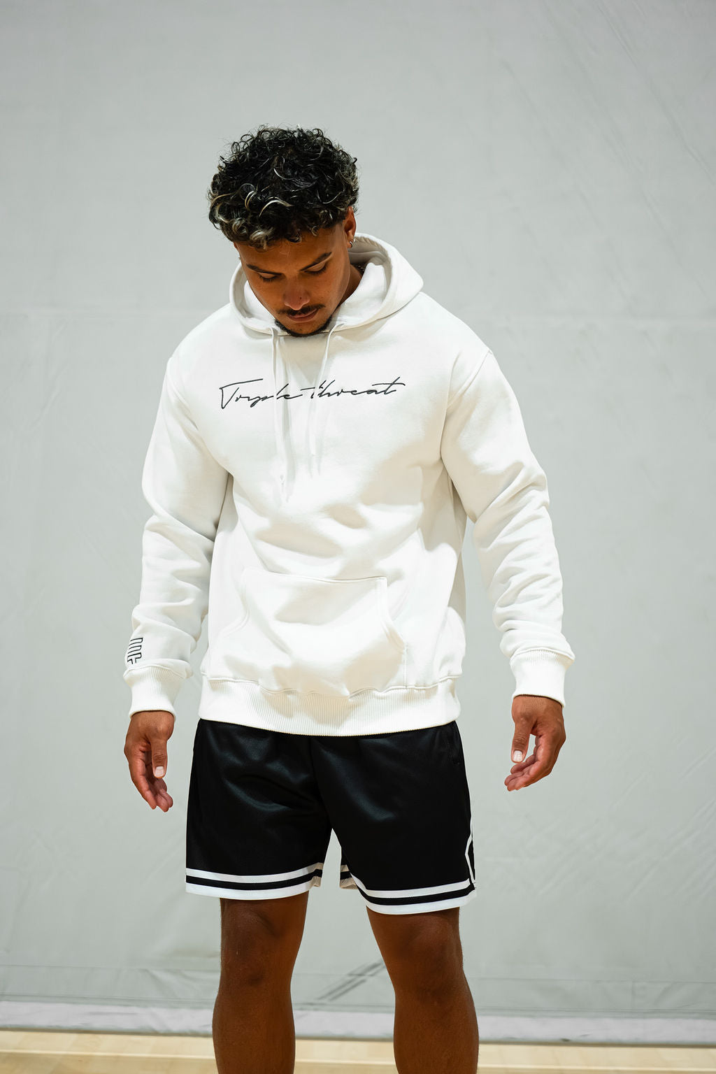 Man wearing a white hoodie with black text and black shorts against a grey background