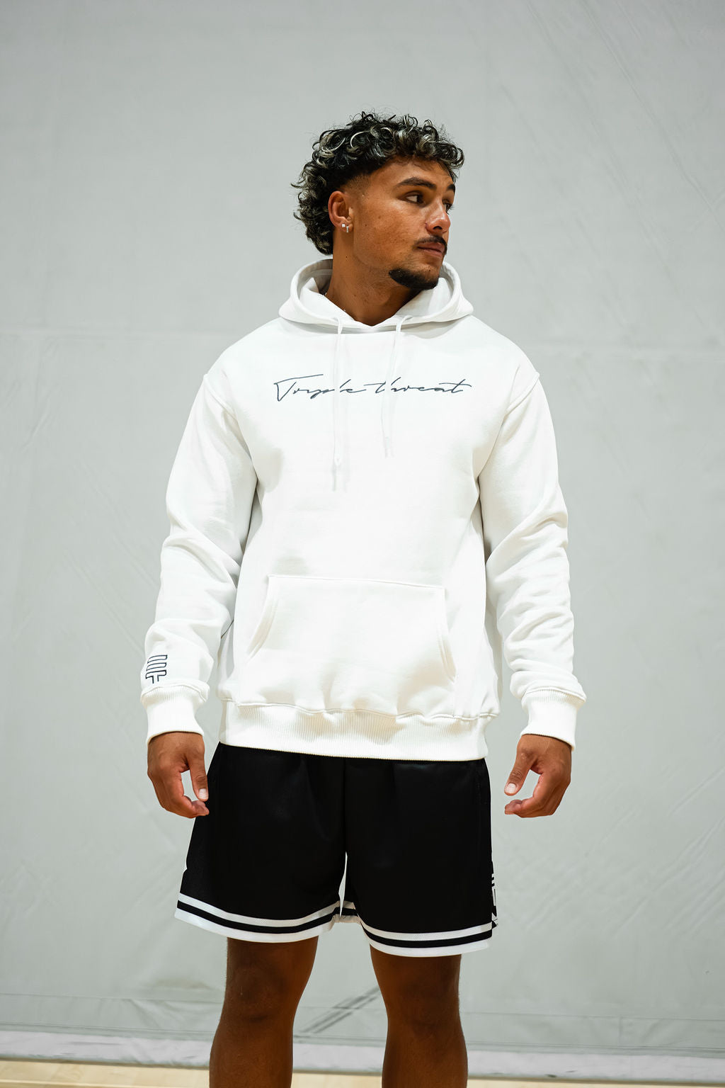 Man wearing a white hoodie with text and black basketball shorts on a grey background